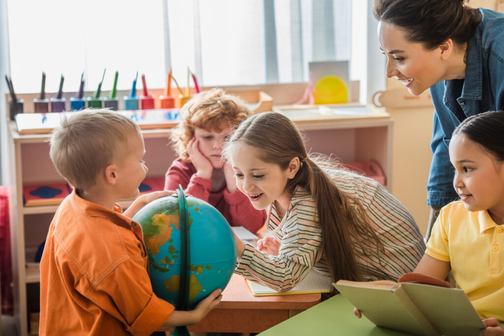 amazed girl looking at globe near interracial friends and teacher - Creative World of Montessori
