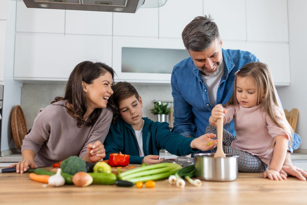 Family of four cooking together in a bright kitchen, chopping vegetables on a wooden table.