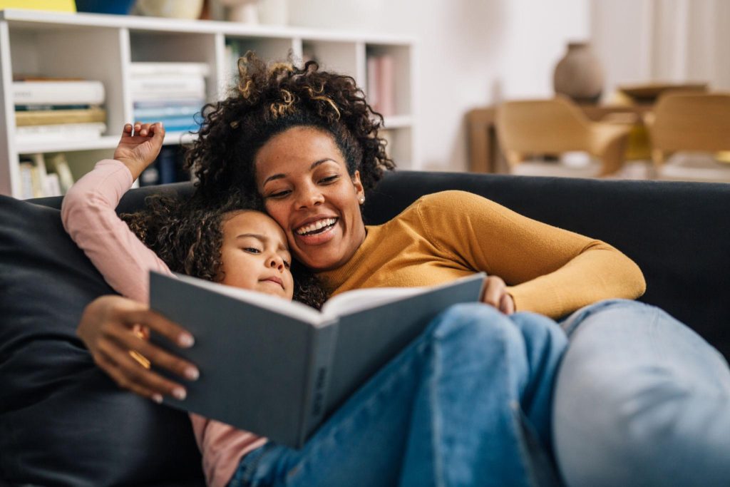 Mother and child cuddling on a sofa while reading a book together in a cozy living room.