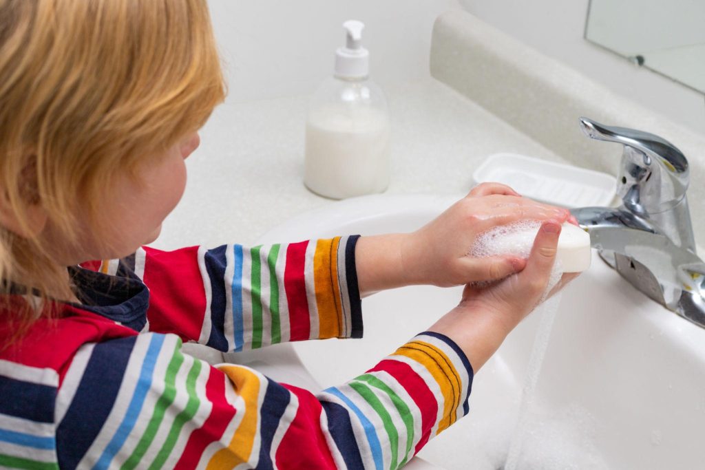 Child washing hands with foamy soap at a bathroom sink with a faucet nearby.